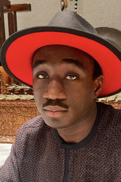 Grad student in a black hat with red underside sitting in front of musical instruments