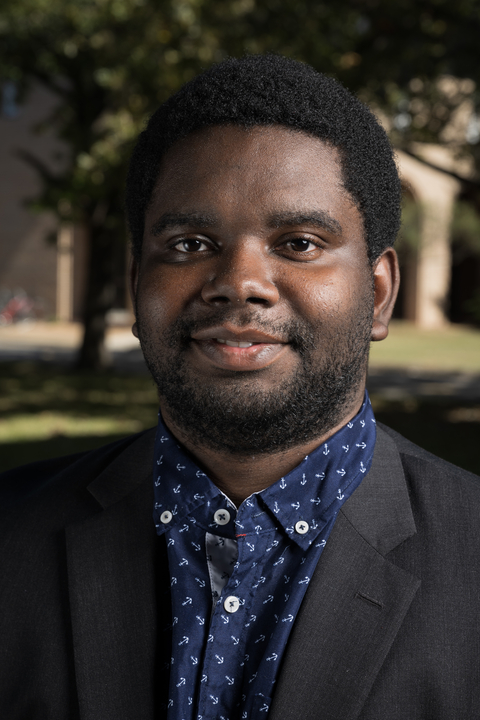 Tam wearing a dark colored suit jacket and a blue collared shirt with a white anchor pattern